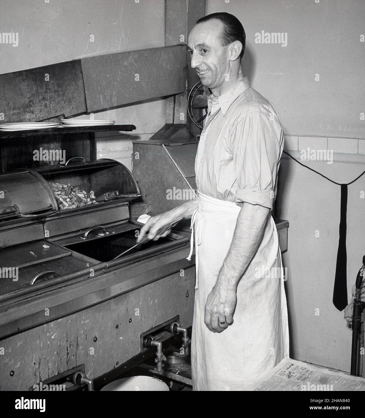 1951, historical, a male cafe owner in his kitchen, wearing a waist or half apron, standing at the fryer cooking food, London, England, UK. Stock Photo
