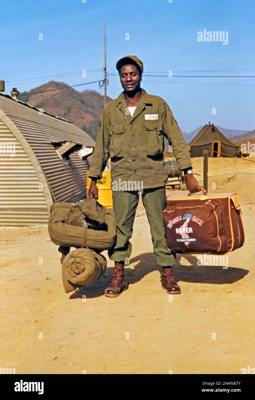 An American soldier ready to return home from his tour of duty in the Korean War in 1953. The black serviceman carries a brand-new kitbag with the slogan ‘To Hell and Back – Korea’. Definitely not military issue, this must have been bought locally as a souvenir of the time spent on active service overseas. This amateur Kodak colour transparency was taken by a fellow serviceman – a vintage 1950s photograph. Stock Photo