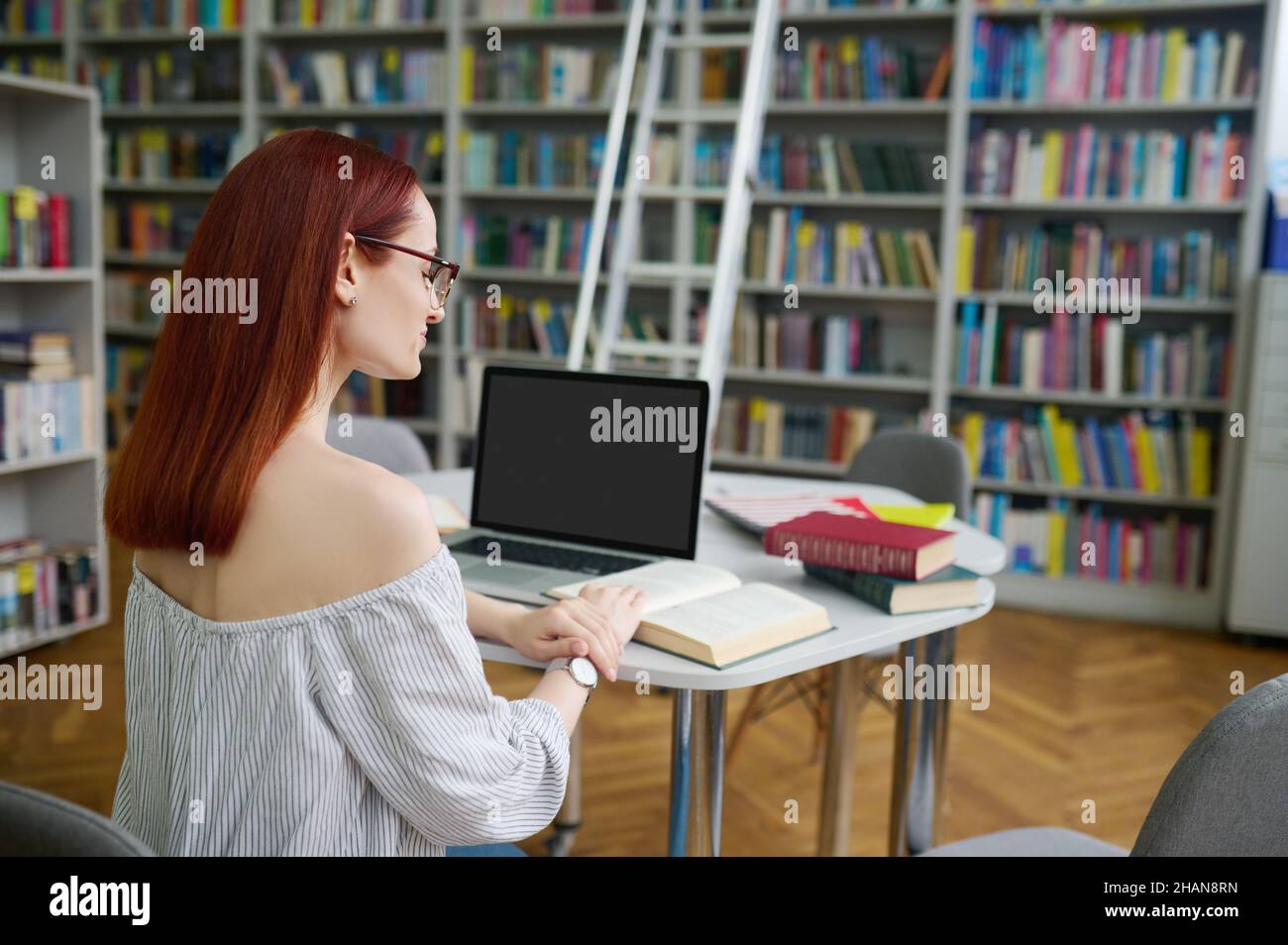 Back view of woman reading book in library Stock Photo