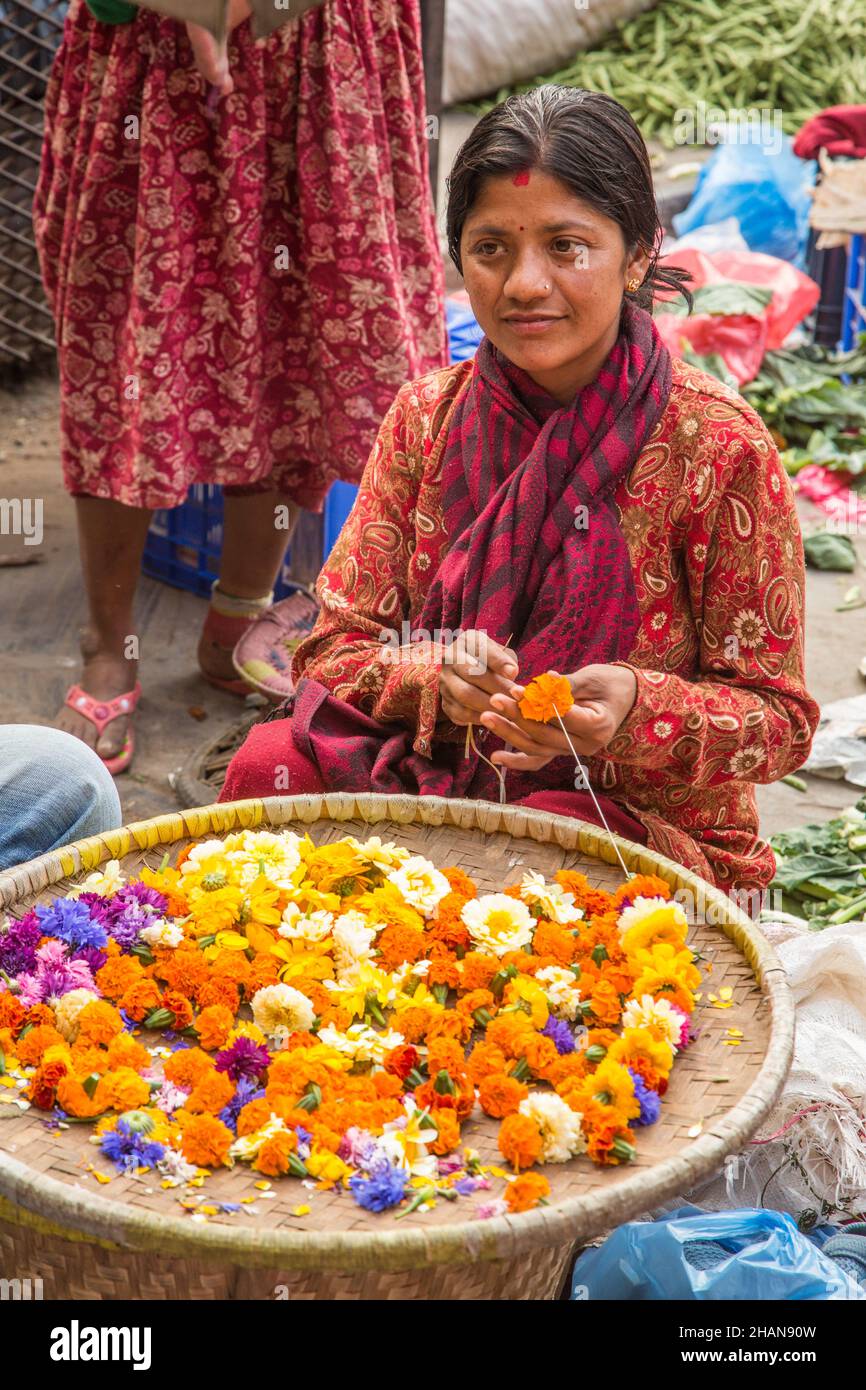 A young Nepali woman making flower garlands for religious offerings at