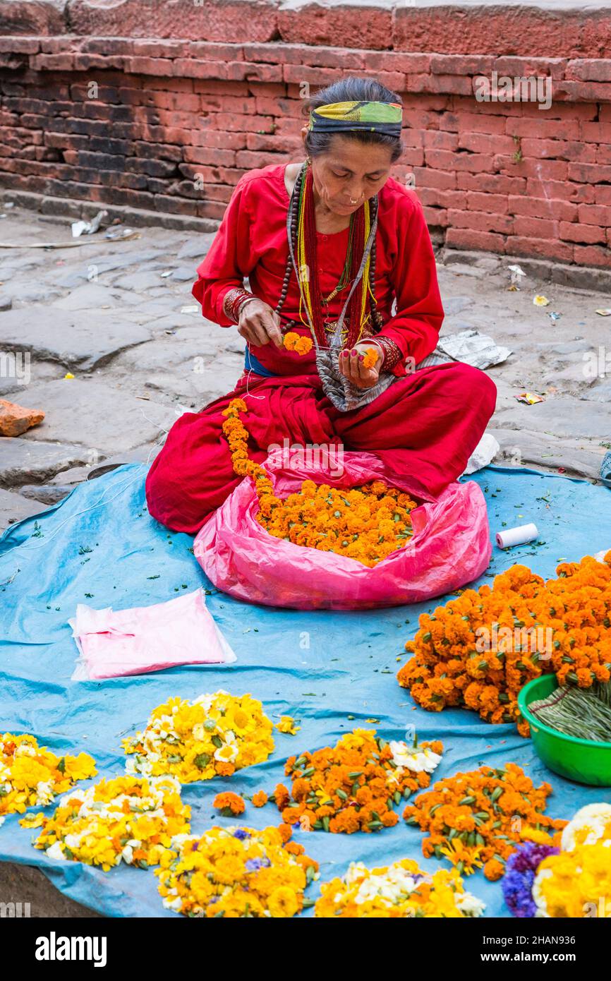 A Nepali woman strings flowers to make garlands for religious offerings