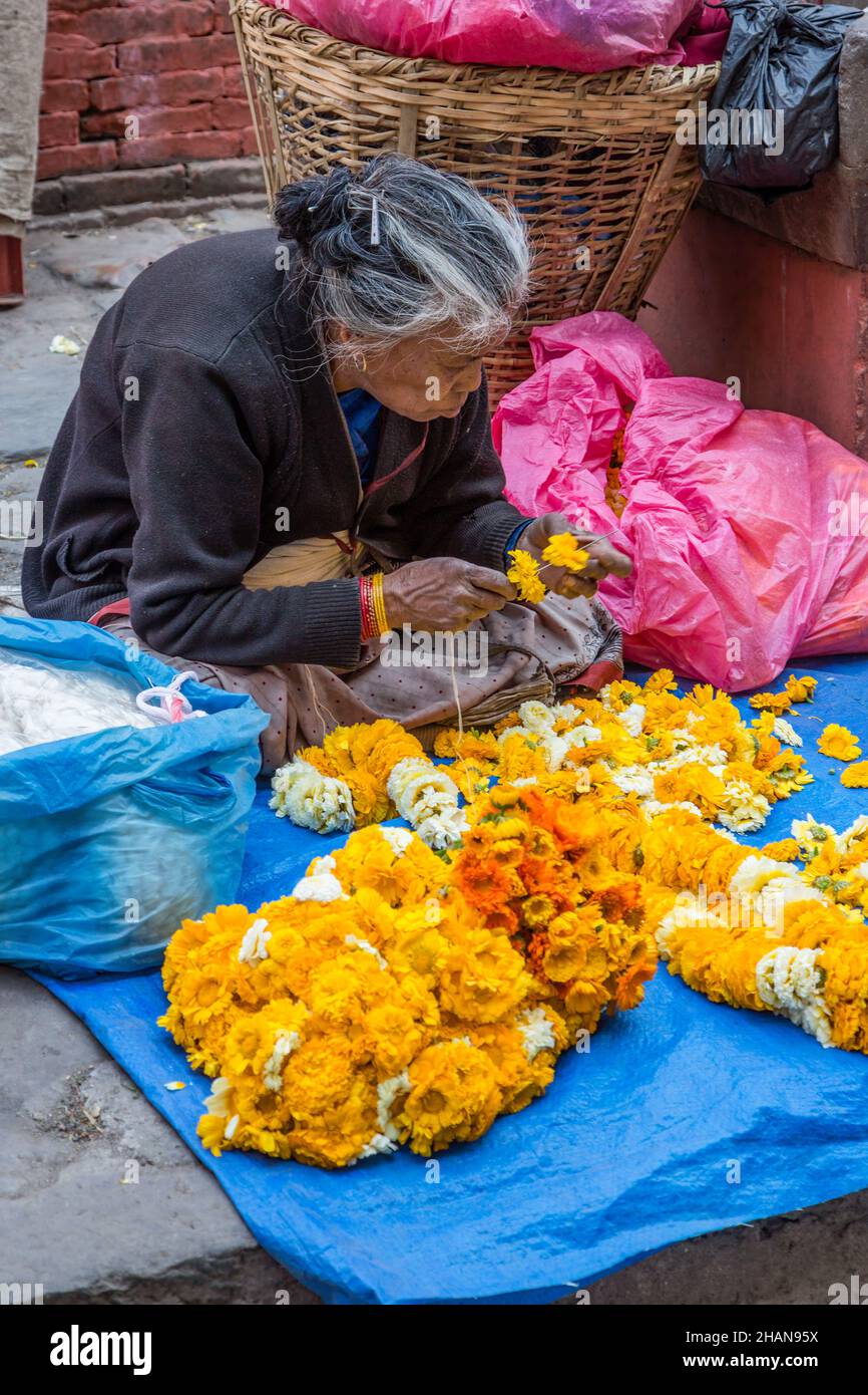 An older Nepali woman strings flowers to make garlands for religious