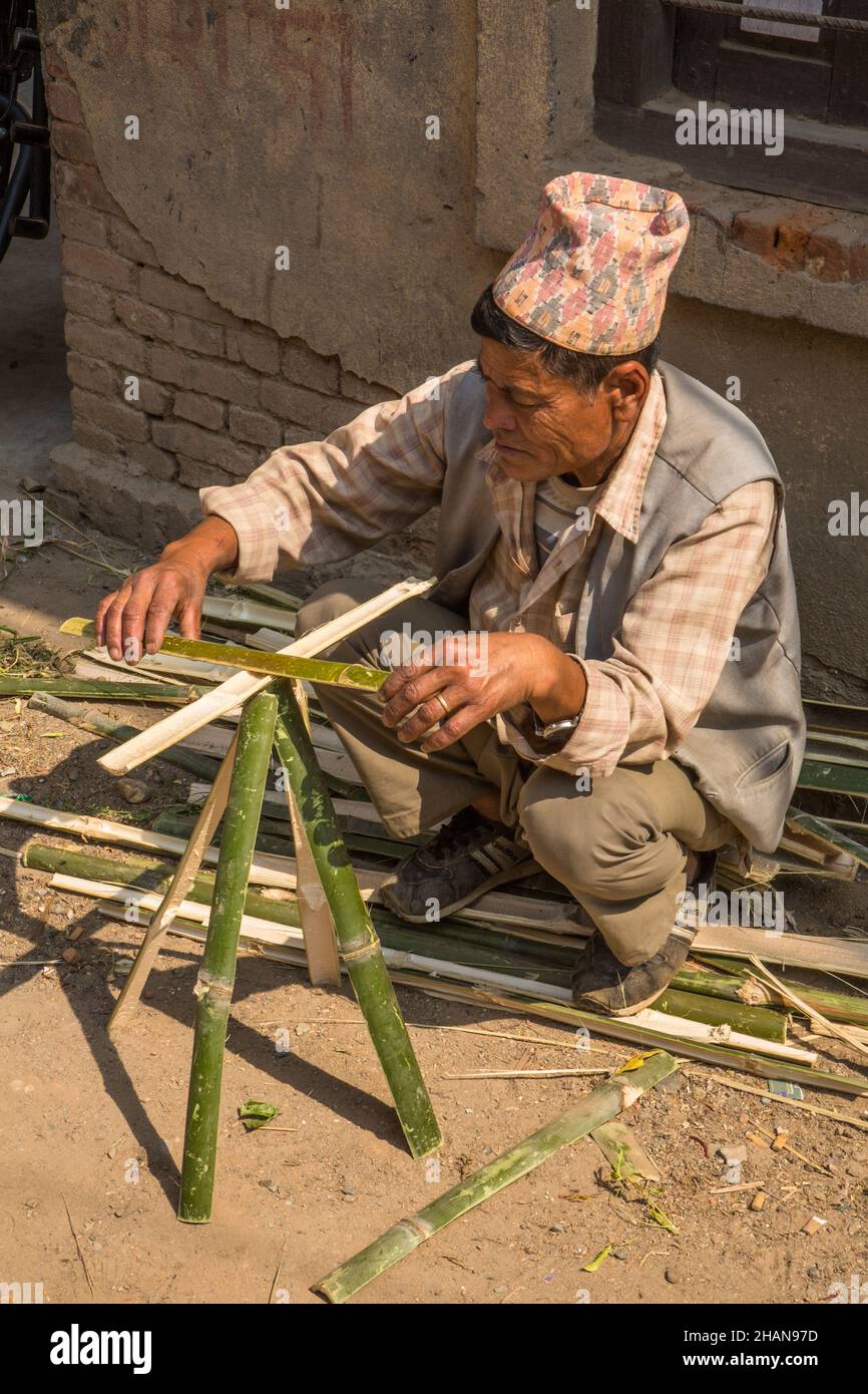 A Nepali man in a dhaka topi hat works with split bamboo in the medieval Newari village of Khokana.  Kathmandu Valley, Nepal. Stock Photo