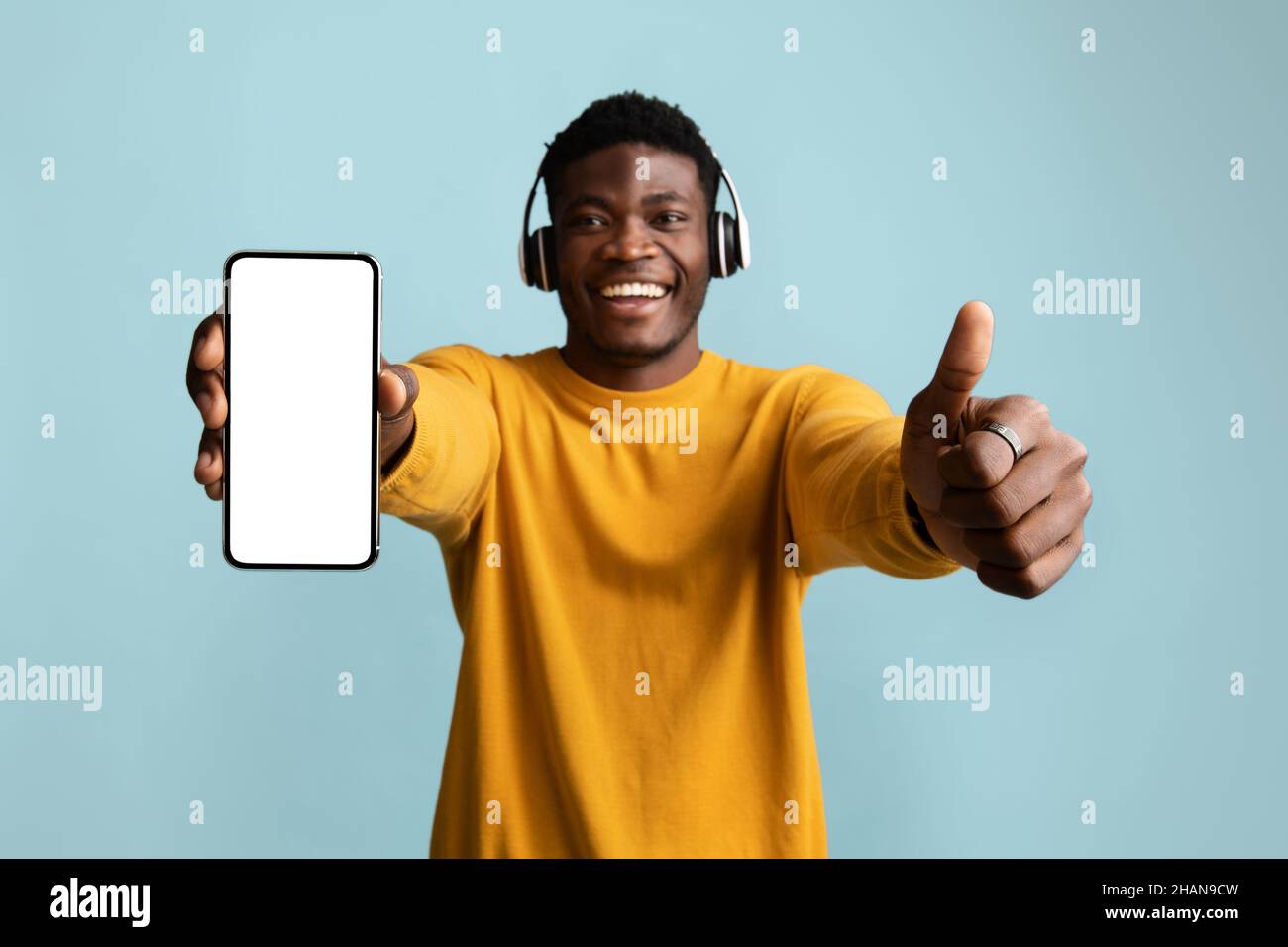Handsome african american young man with headphones showing cellphone, mockup Stock Photo