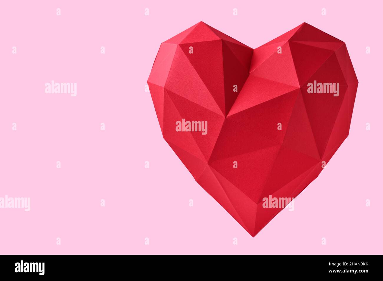 Red paper hearth isolated on pink background. Red polygonal paper heart for Valentine's day or any other Love invitation cards. Top view, copy space. Stock Photo