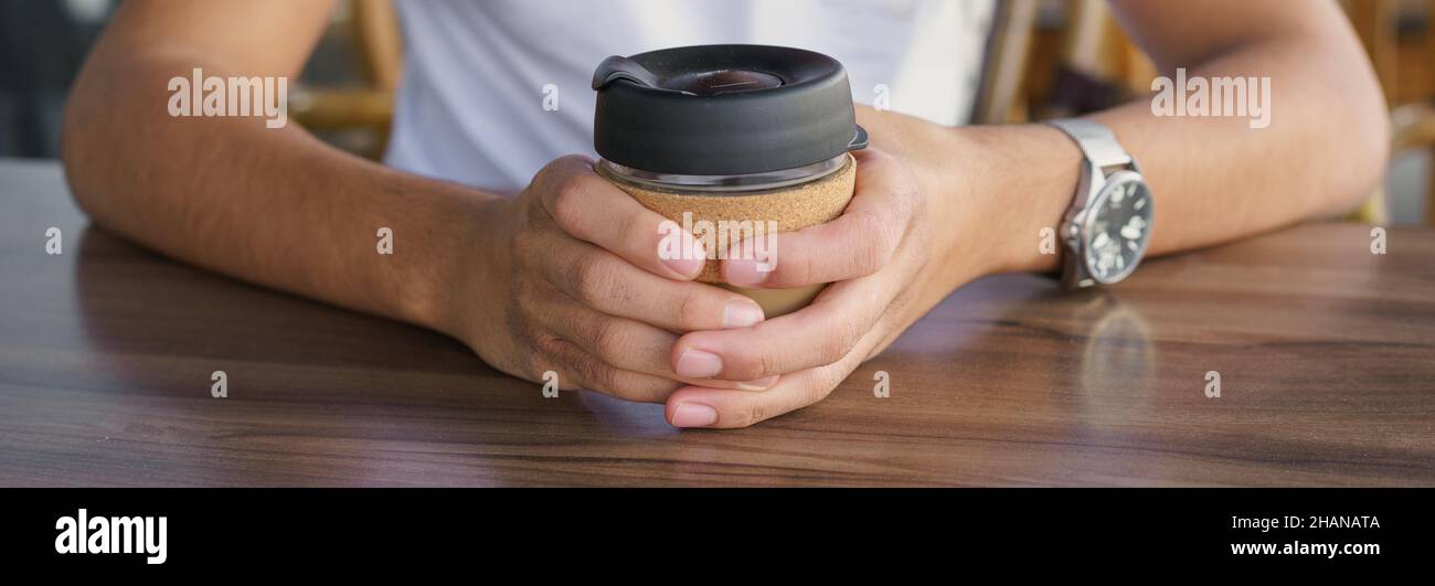 Banner male hands hold reusable coffee mug. Young man drink coffee from reusable travel coffee cup. Teenager holding reusable coffee mug. Sustainable lifestyle. Eco friendly concept. Stock Photo