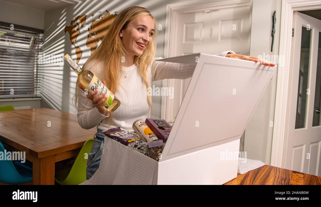 A young 22 years female smiling after receiving a gift box hamper for a life celebration event at home in a bright sunshine lit home. Stock Photo