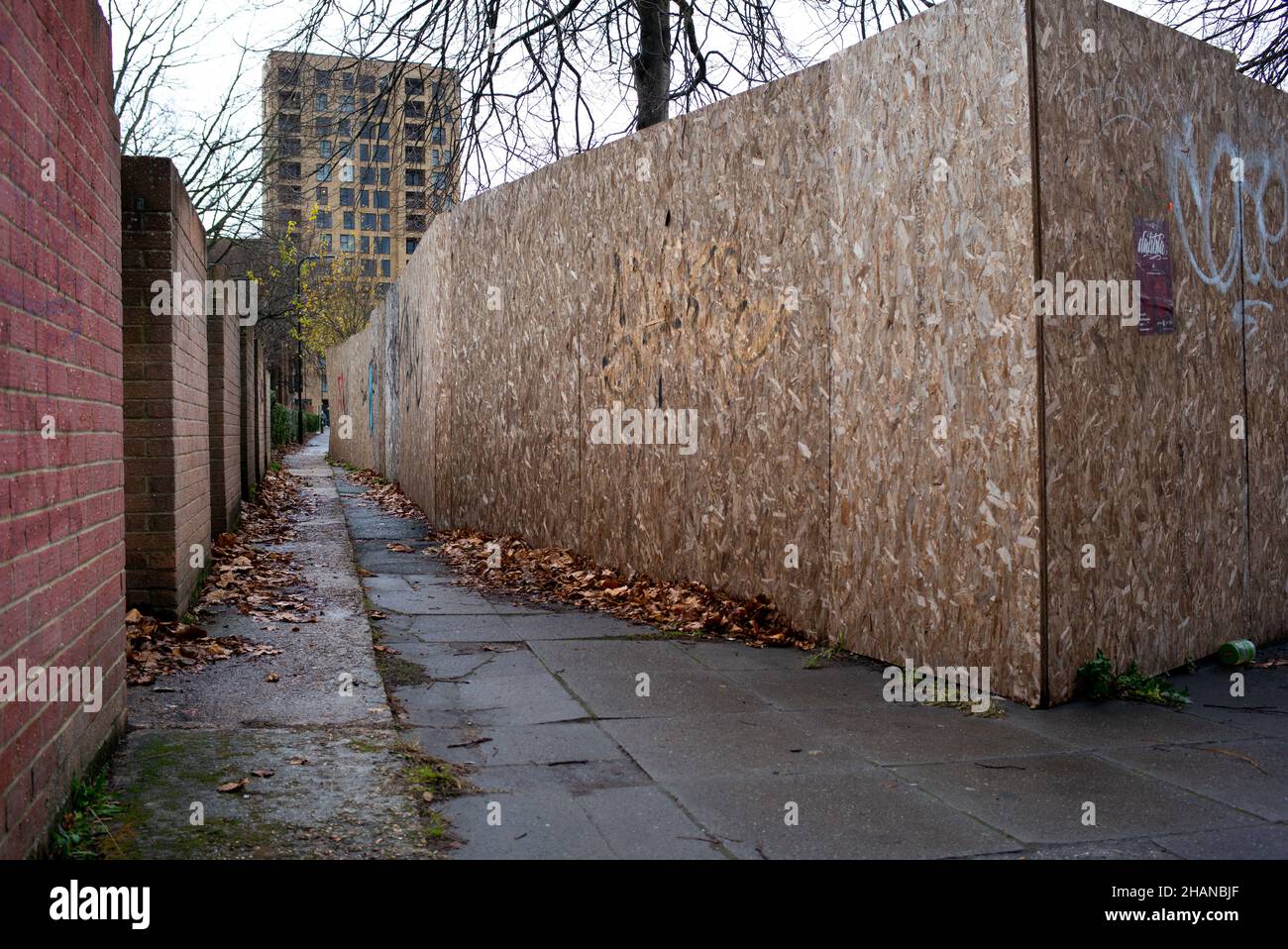 A city alleyway with one side brick wall the other chipboard from a building site creating an eerie scene which could be used in a conceptual way. Stock Photo