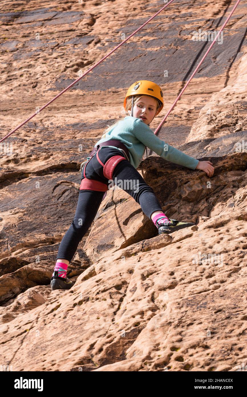 A seven-year old girl learning to rock climb at the Wall Street climbing area near Moab, Utah.  She is looking down at her mother below for guidance a Stock Photo