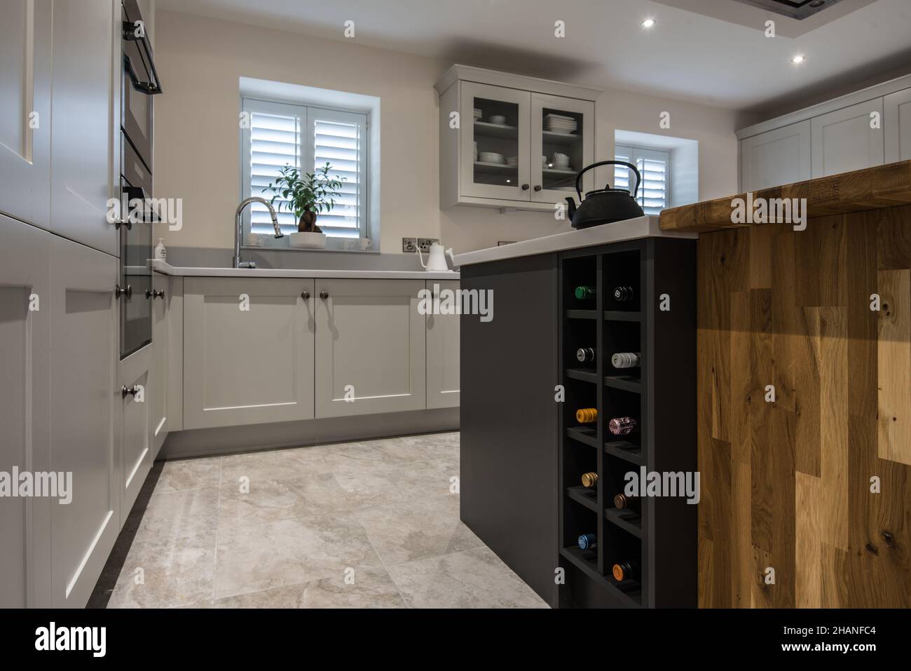 A light,contemporary, fitted kitchen with a wine rack,island,blinds (using mixed materials including blockwood).Has kitchen island with extractor fan. Stock Photo