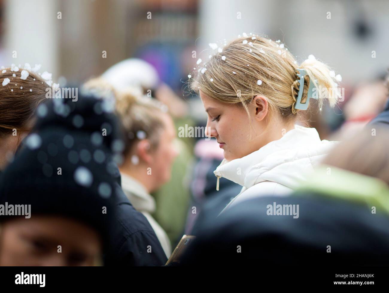 Flakes of artificial snow are seen on the heads of people gathering in