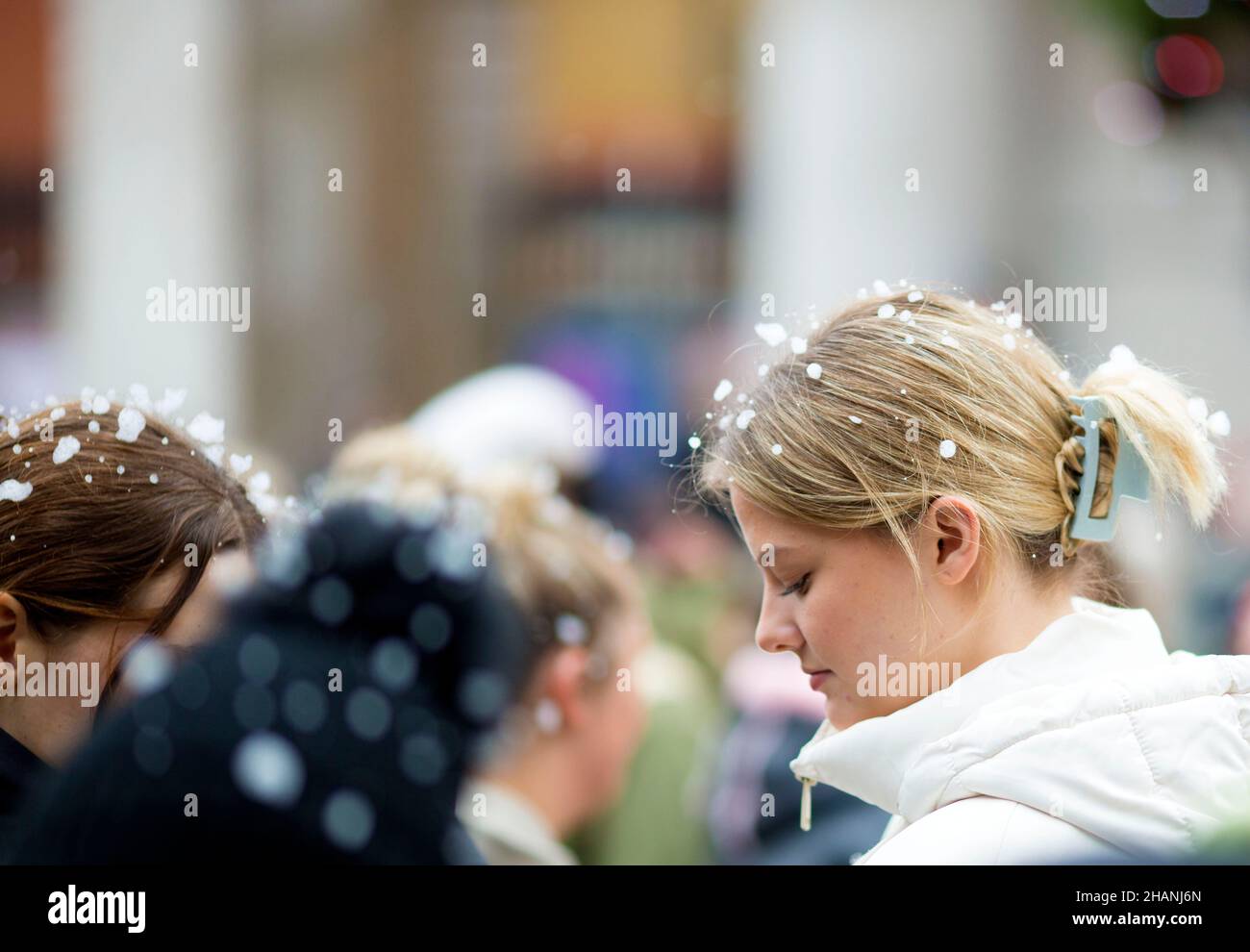 Flakes of artificial snow are seen on the heads of people gathering in Covent Garden in central