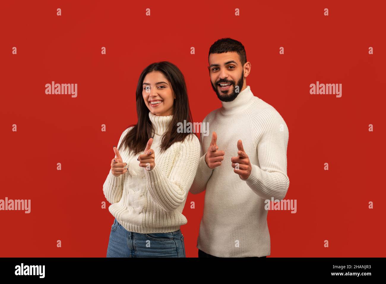 Your turn. Happy middle eastern couple pointing at camera with fingers, picking somebody, posing over red background Stock Photo