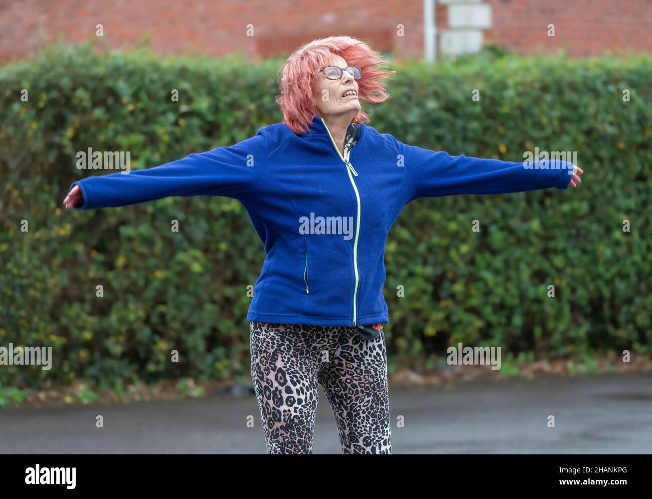 Elderly senior woman in her 80s exercising outside doing star jumps in Winter. Old lady keeping an active healthy lifestyle. Stock Photo