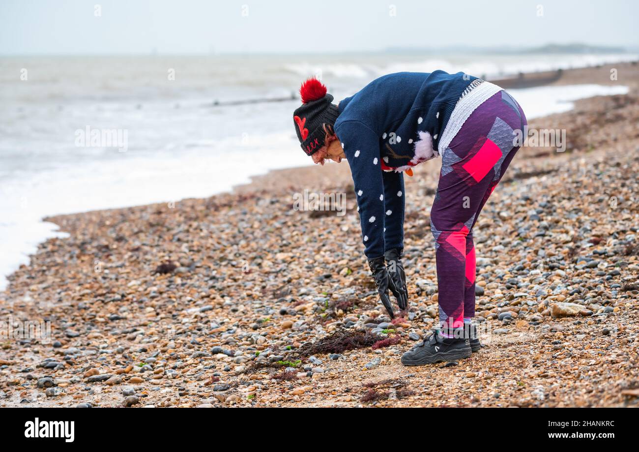 Elderly senior woman in her 80s on a beach by the sea exercising in Winter. The old lady is wearing a Christmas jumper & hat on the South Coast, UK. Stock Photo