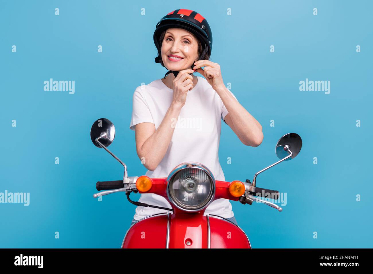 Portrait of attractive cheerful woman fixing helmet riding motor bike isolated over bright blue color background Stock Photo