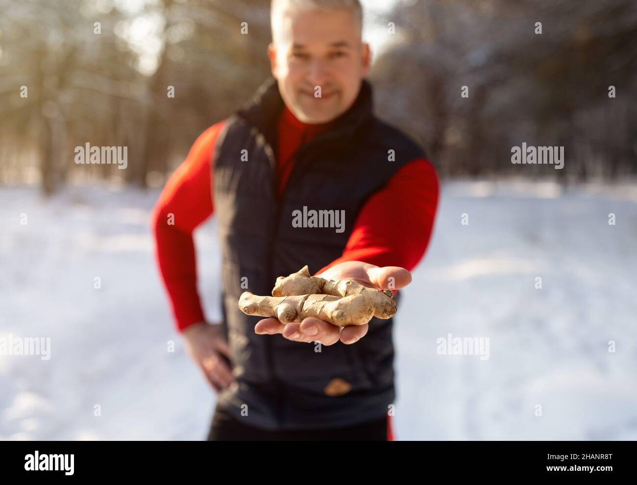 Fit mature man holding ginger root in winter forest, promoting active lifestyle and natural health care, selective focus Stock Photo