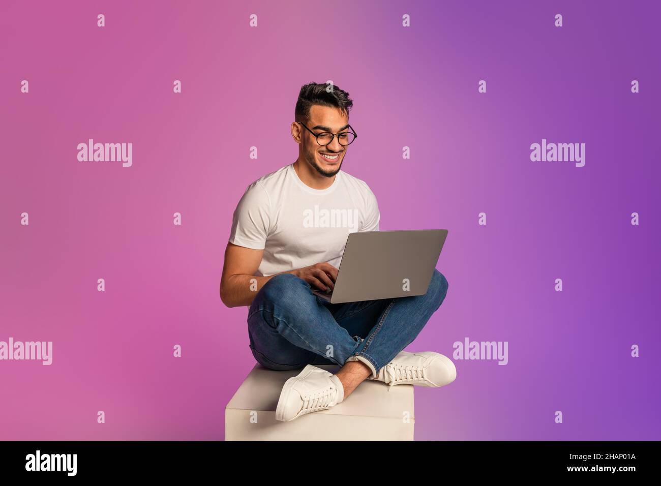 Full length of young Arab man sitting cross legged with laptop, having ...