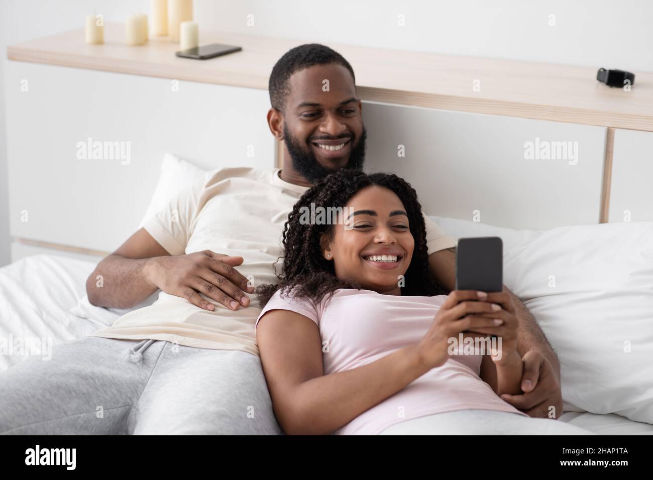 Cheerful young african american husband hugs wife with smartphone on ...
