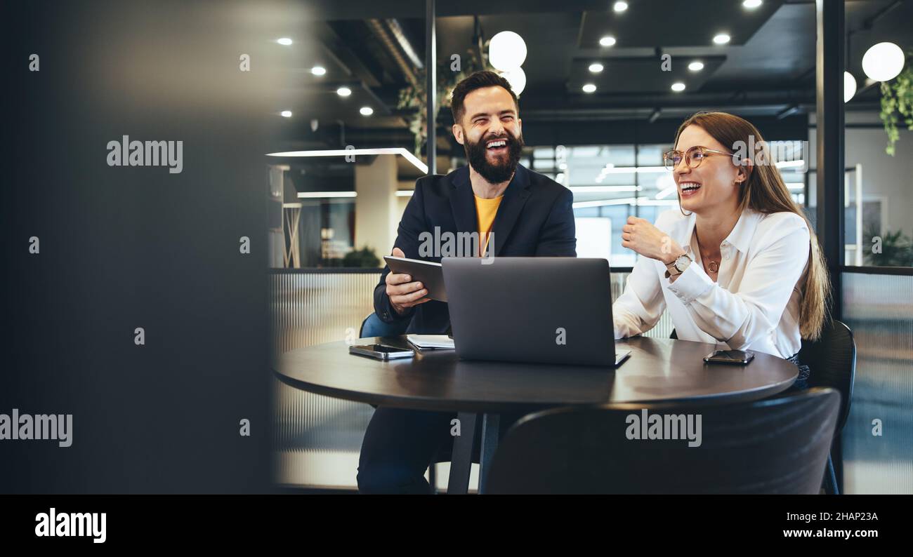 Two happy young businesspeople working together in a modern workspace. Two young entrepreneurs smiling cheerfully while working with wireless technolo Stock Photo