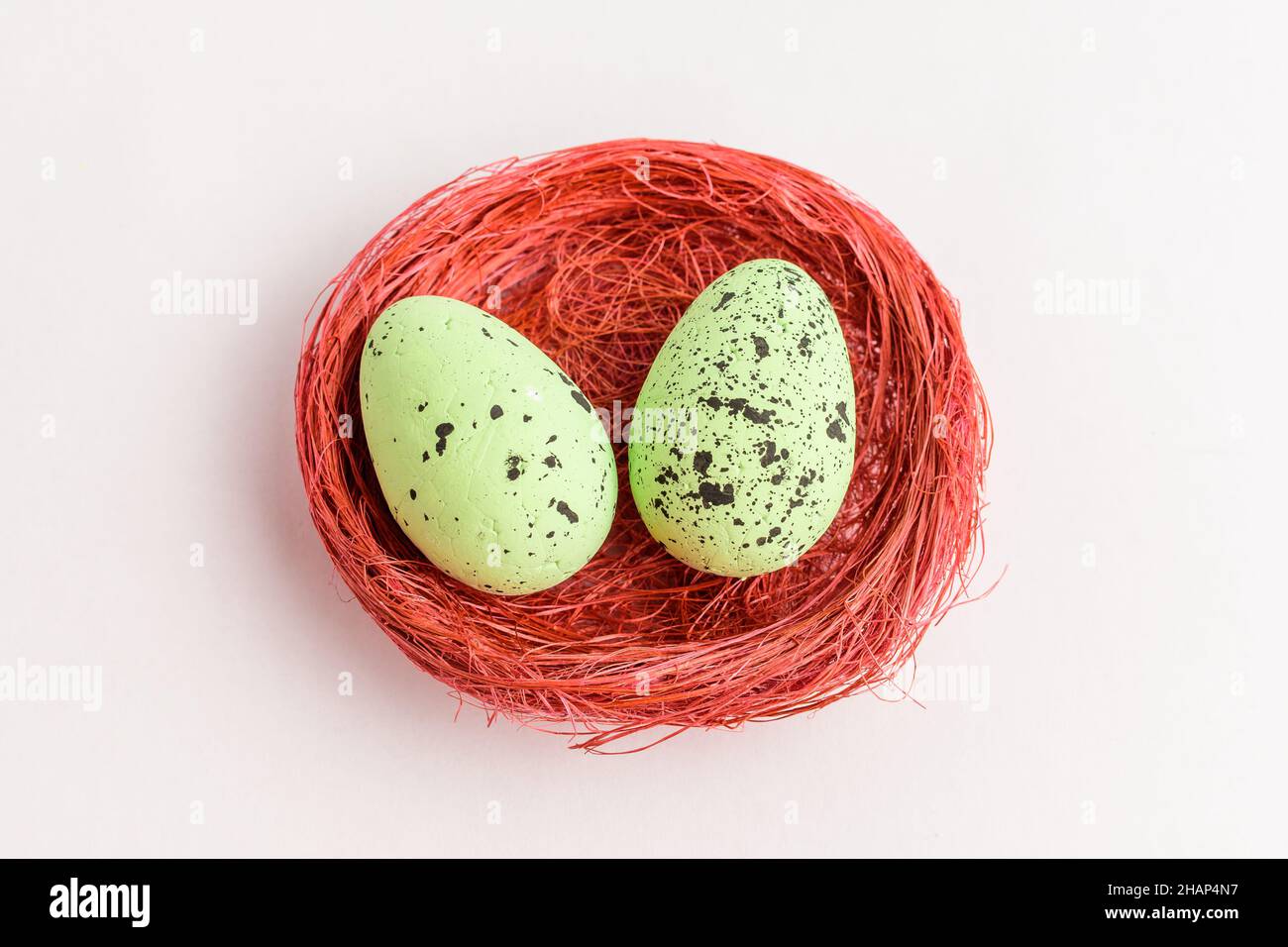 Two green colored decorative Easter eggs in a red rustic basket isolated on a white table Stock Photo