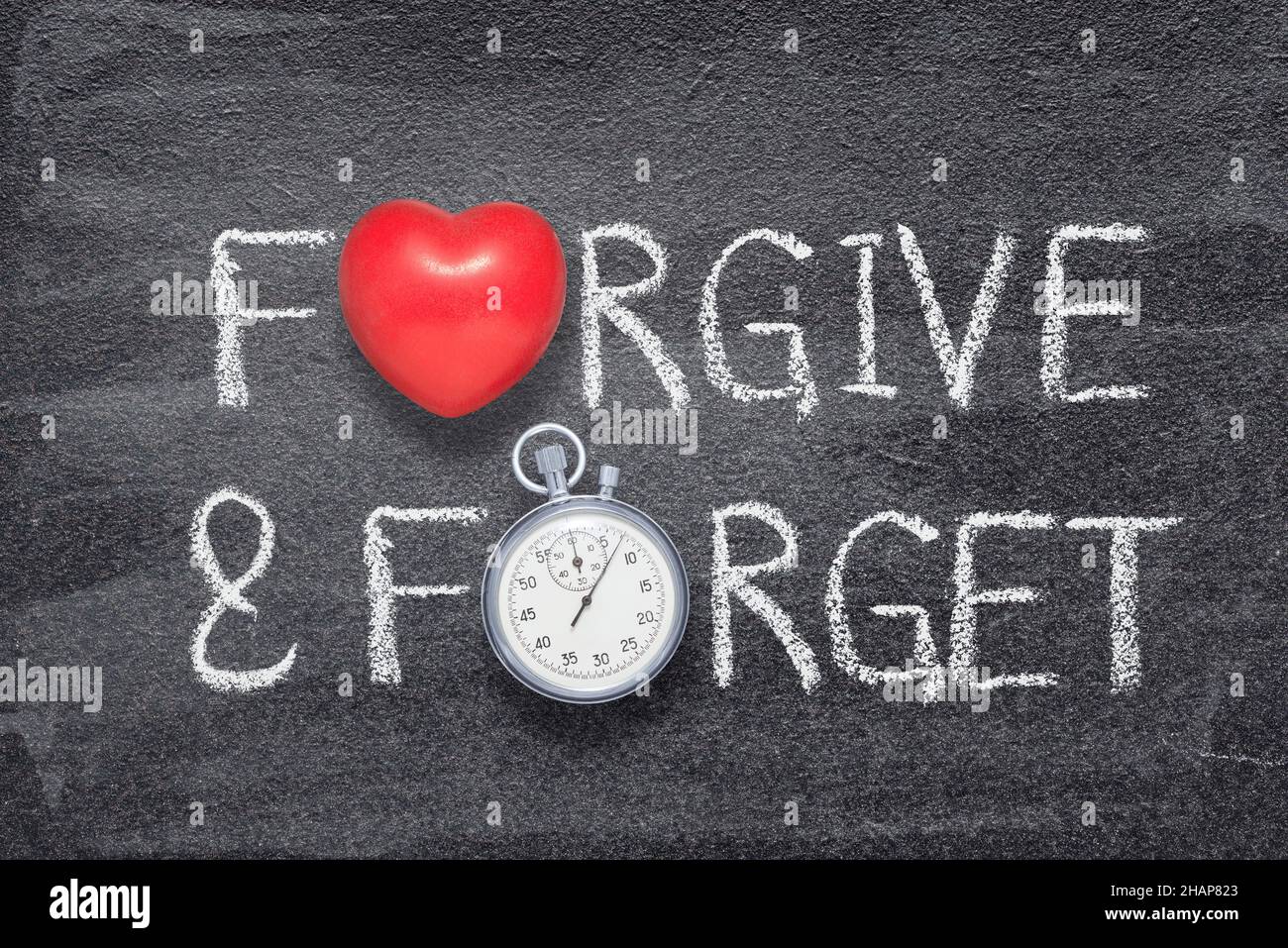 forgive and forget words written on chalkboard with vintage precise stopwatch and red heart symbol Stock Photo