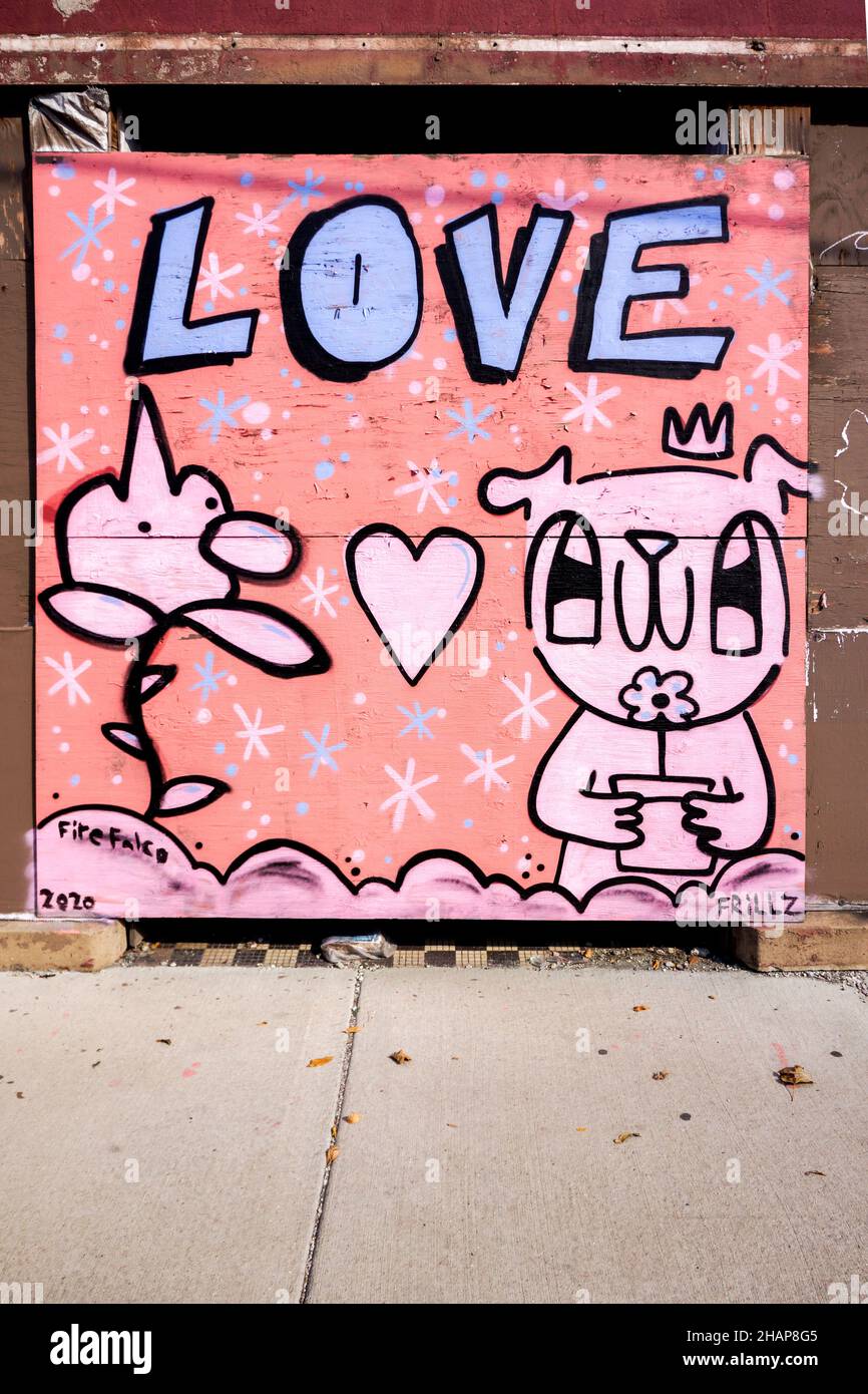 Graffiti wall with the word LOVE painted in lavender and black with a cartoon character holding a flower painted on a plywood board. Stock Photo