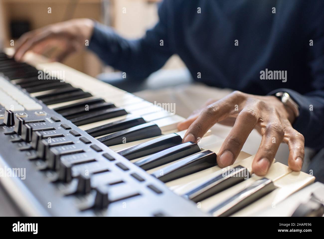 Fingers of young African man pressing keys of piano keyboard while