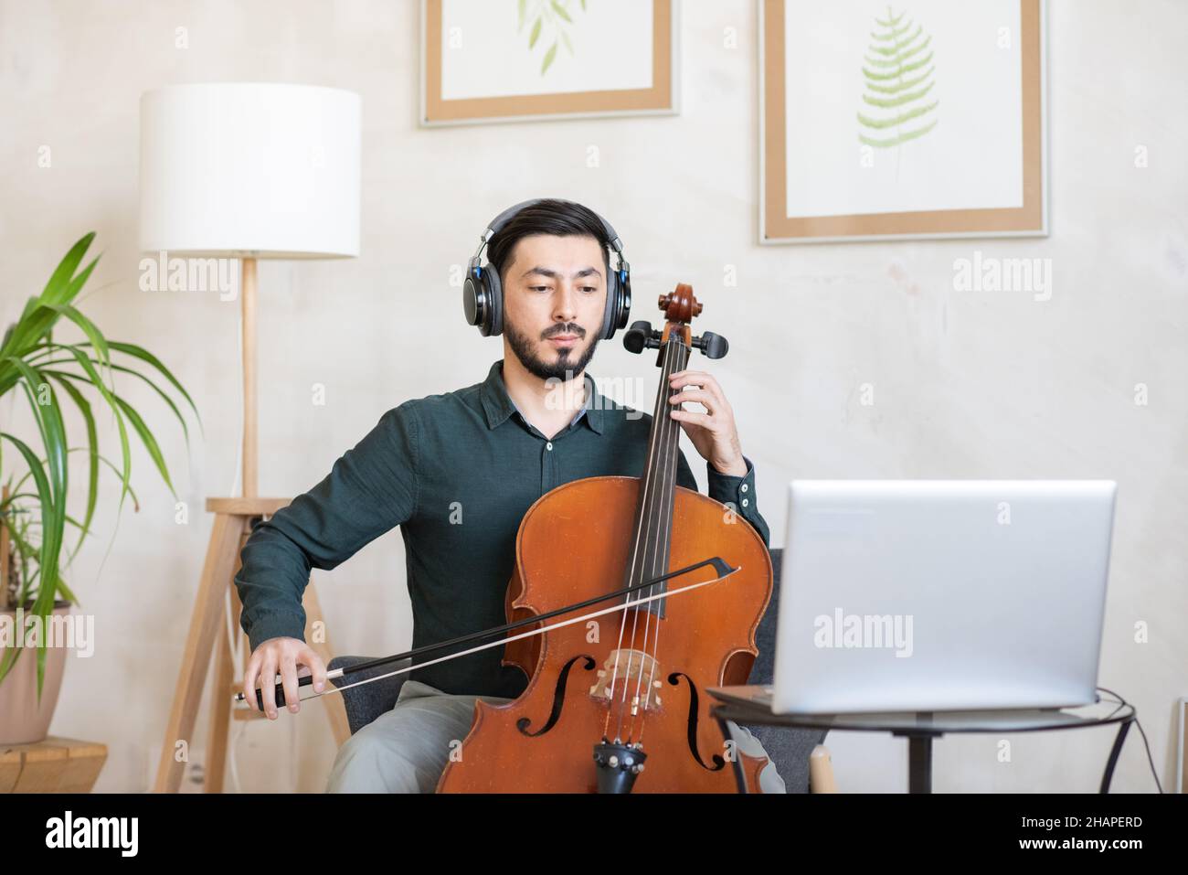 Young confident teacher of music in headphones playing string musical instrument during online lesson Stock Photo