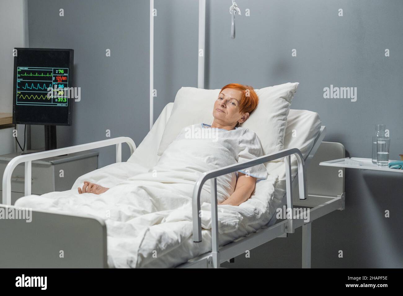 Elderly sick woman with sad expression lying in hospital bed after operation Stock Photo