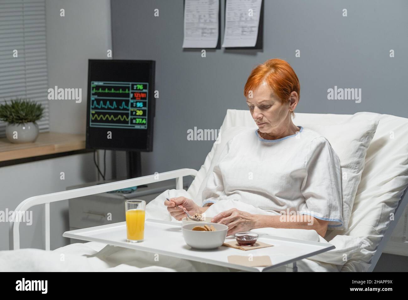 Elderly woman sitting in bed with the tray of food and eating breakfast