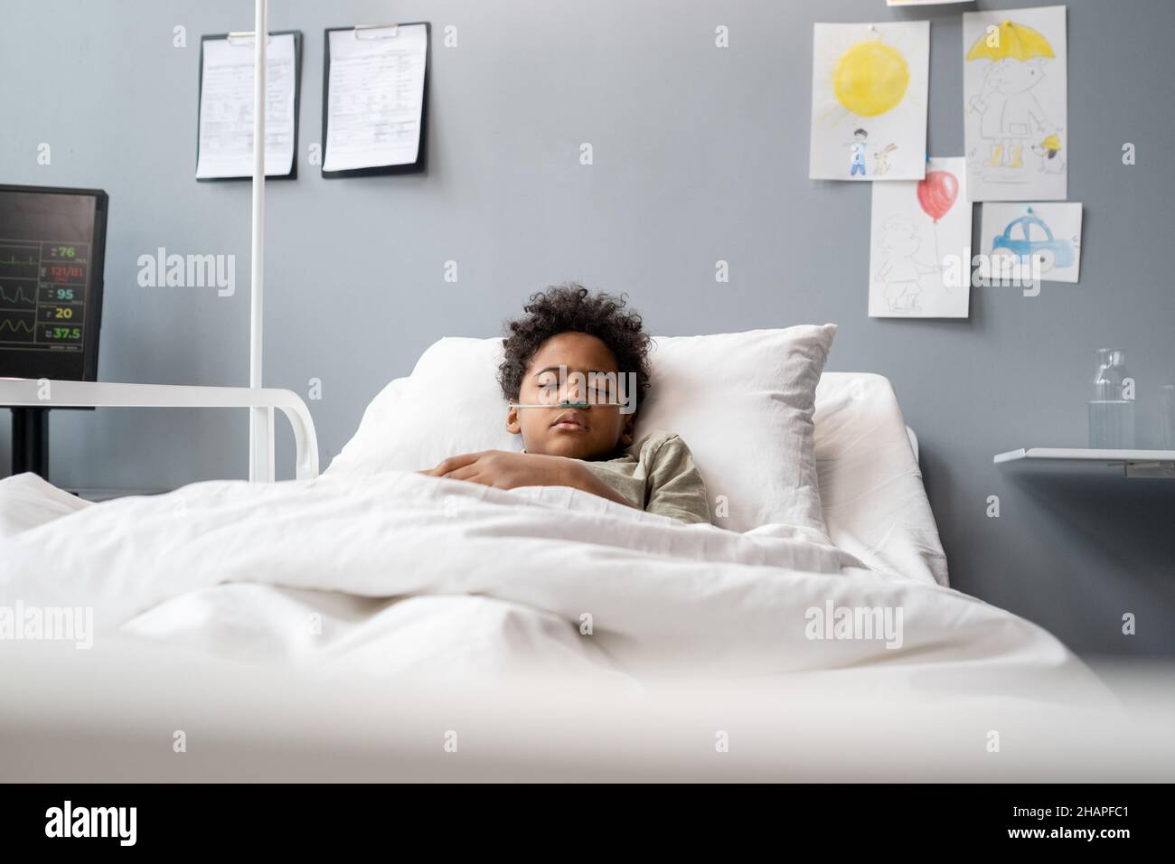 Little boy breathing with oxygen tube in his nose while sleeping in bed and holding treatment at hospital Stock Photo