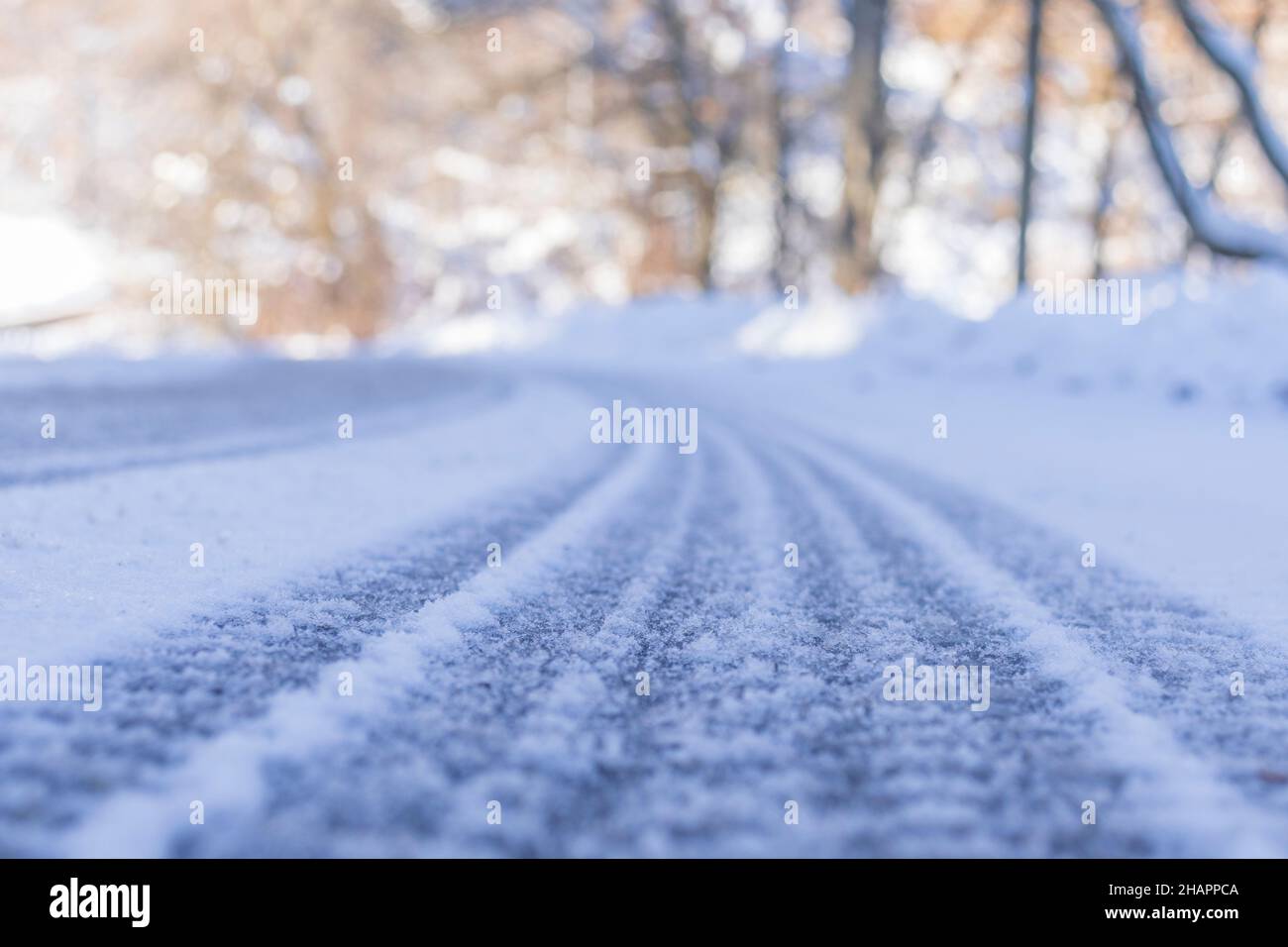 Low angle view on an asphalt road covered with snow leading to a left turn. Trees in the background. Diminishing perspective. Selective focus. Copy sp Stock Photo