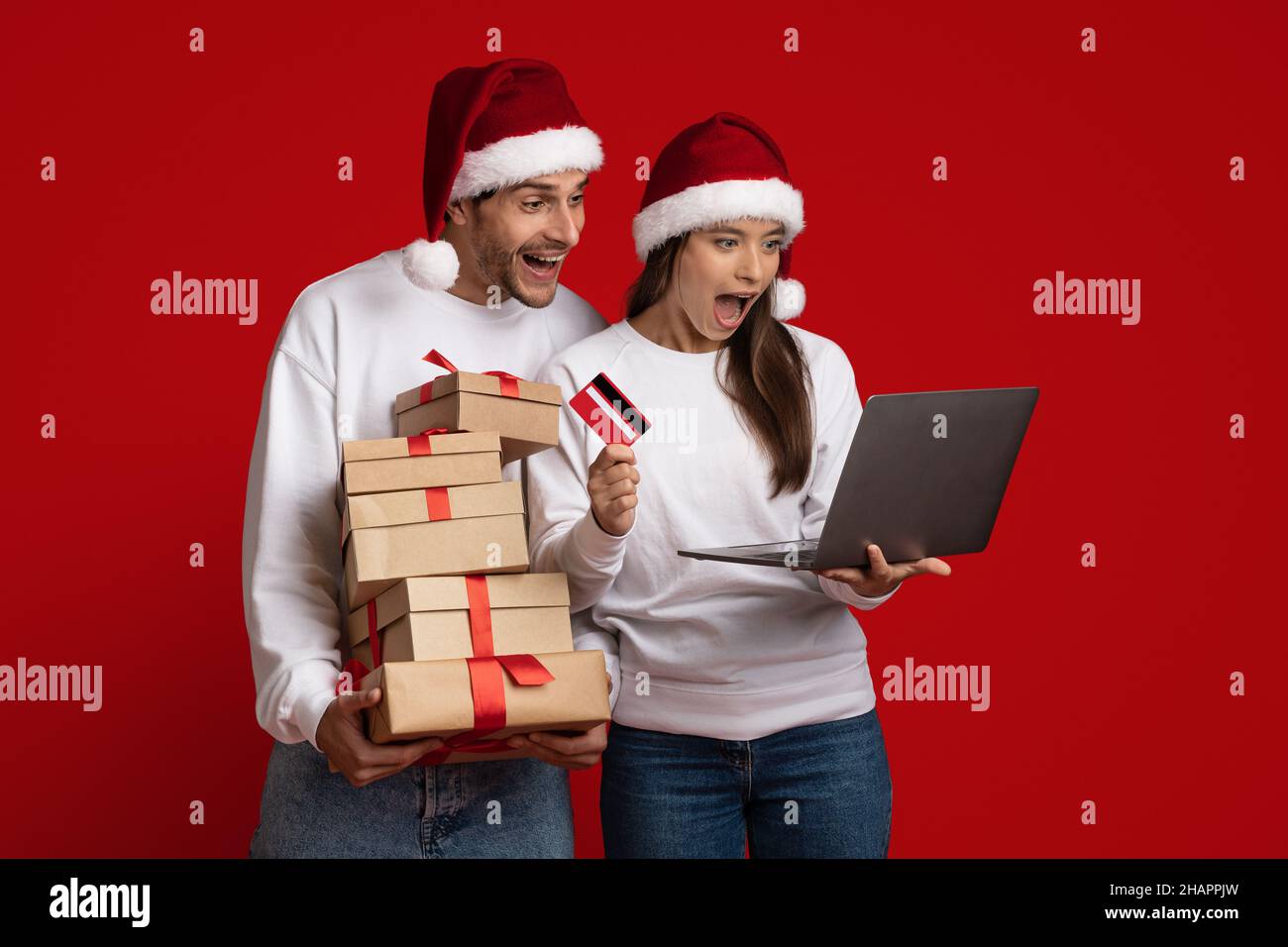 Online Sales. Surprised couple wearing santa hats using laptop and credit card Stock Photo