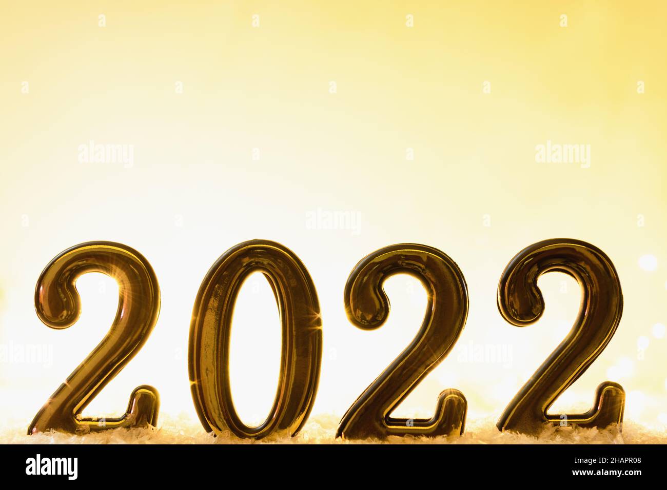 Gold numbers 2022 on yellow background with snow and luminous yellow garland. New year backdrop with 2022 year Stock Photo