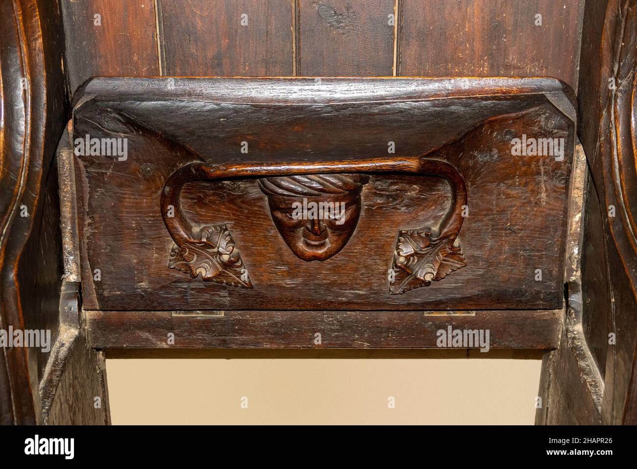 A friendly face carving on the underside of a misericord church seat in the upright position. At St Mary of the Assumption, Ufford, Suffolk Stock Photo