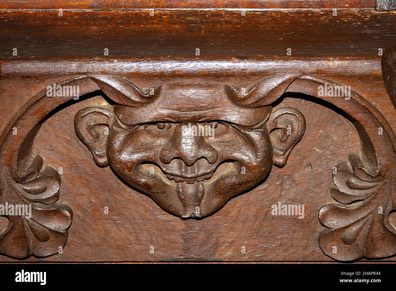 A demonic face carving on the underside of a misericord church seat in the upright position. At St Mary of the Assumption, Ufford, Suffolk Stock Photo