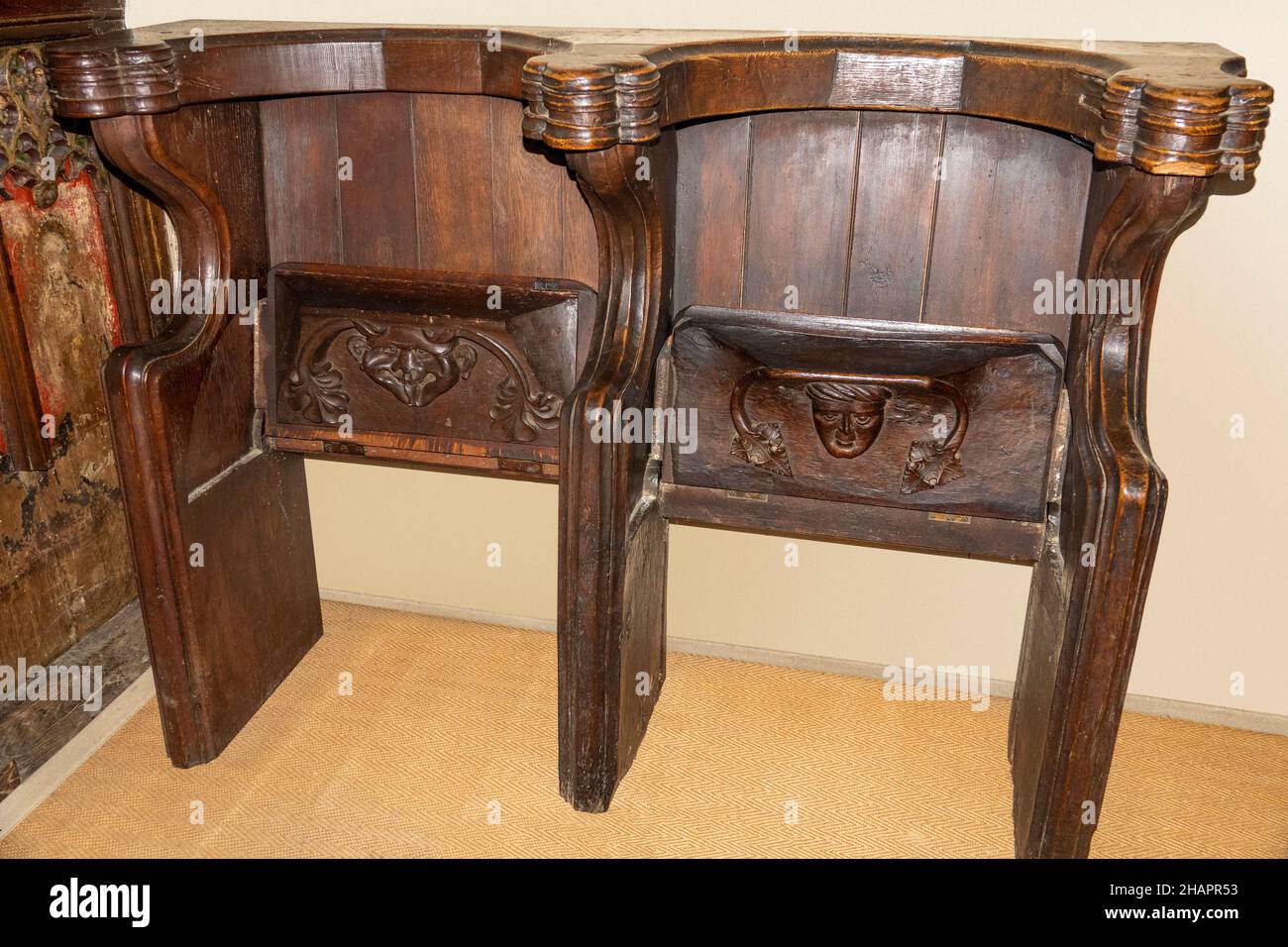 A double place misericord church seat in the upright position showing the two carved faces. One demonic. At St Mary of the Assumption, Ufford, Suffolk Stock Photo