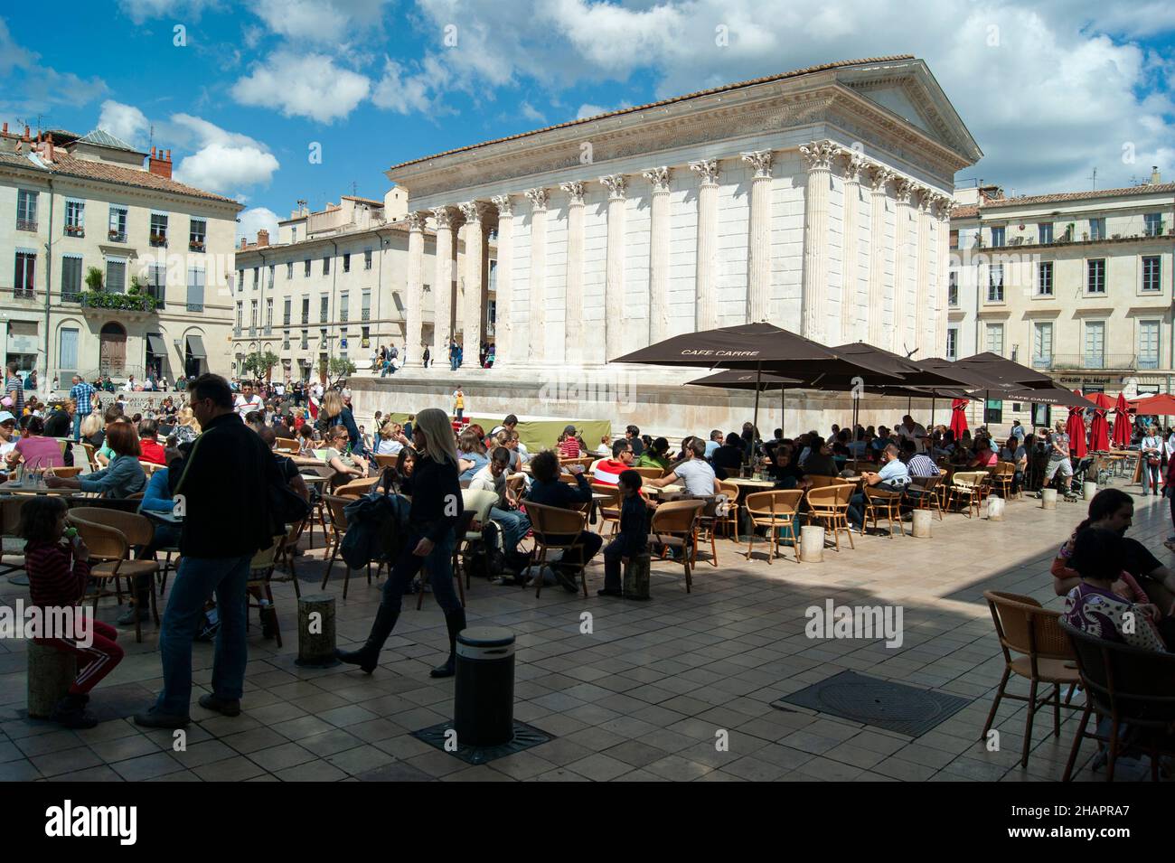 Nimes - France - April 24 2011 : Beautiful historic Maison Carree, a classical Roman temple. Holidaymakers enjoy a spring day at pavement cafes. Lands Stock Photo