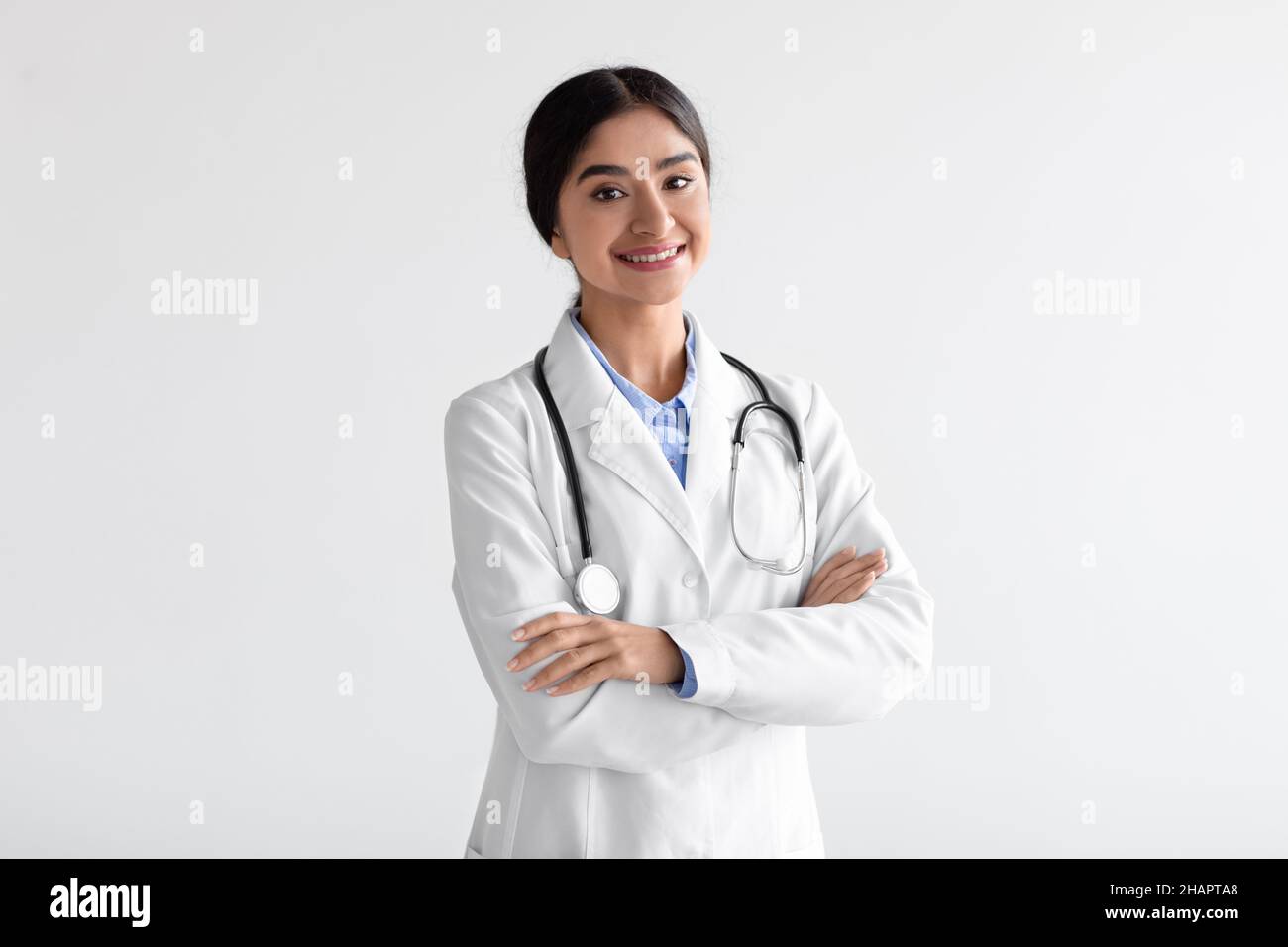 Happy friendly attractive young indian woman doctor in white coat with stethoscope with crossed arms on chest Stock Photo