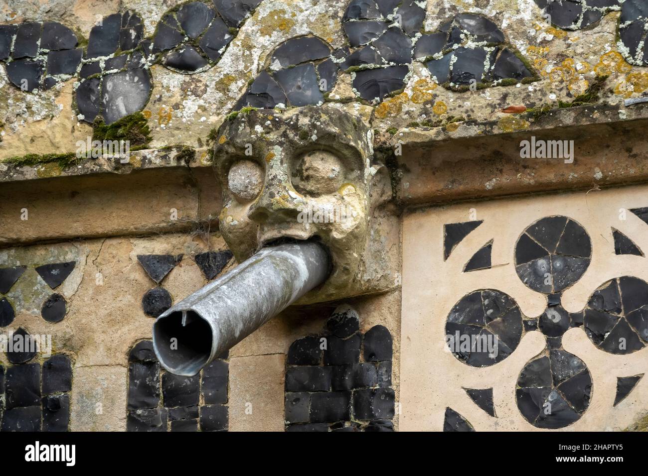Example of intricate flint flushwork on an exterior wall with gargoyle waterspout at St Mary of the Assumption, Ufford, Suffolk Stock Photo