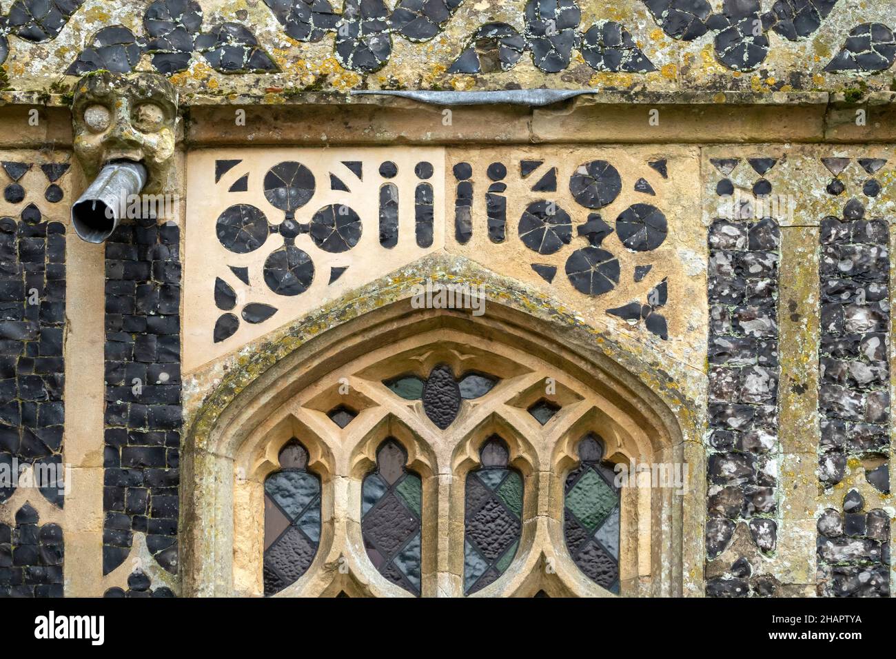 Example of intricate flint flushwork on an exterior wall with gargoyle waterspout at St Mary of the Assumption, Ufford, Suffolk Stock Photo