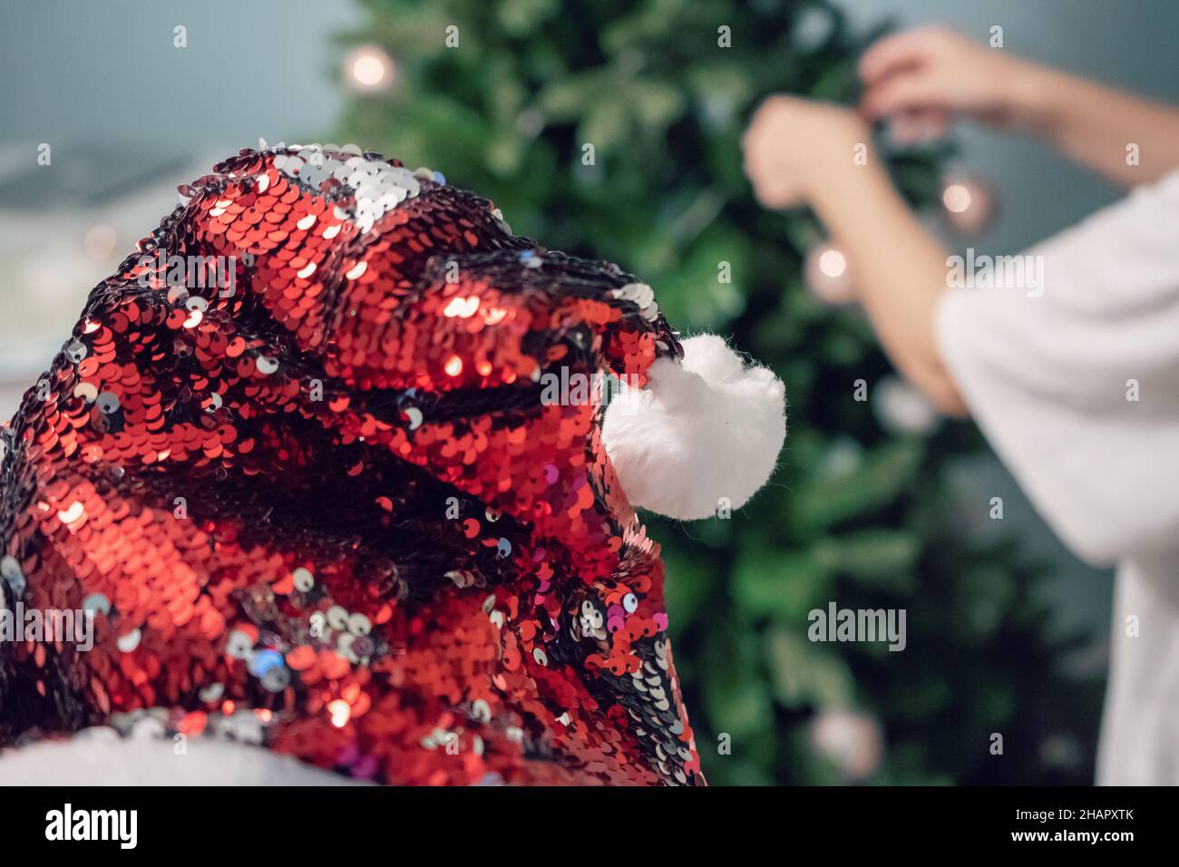 Women's hands decorate the Christmas tree with balls and toys. Red Santa Claus Hat on Christmas tree. New Year mood. Party and holiday celebration con Stock Photo