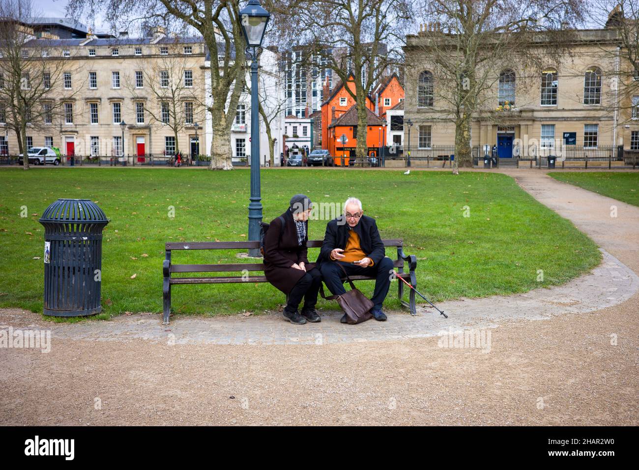Old couple sat on a park bench using a smartphones Stock Photo
