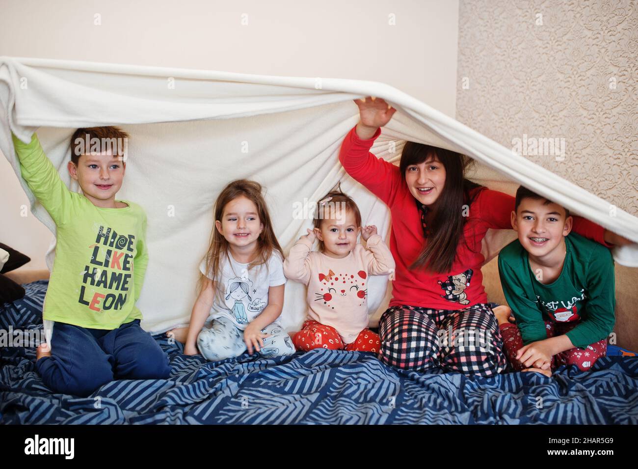 Happy big family is having fun together in bedroom. Large family morning concept. Mother with four kids wear pajamas in bed at home. Stock Photo