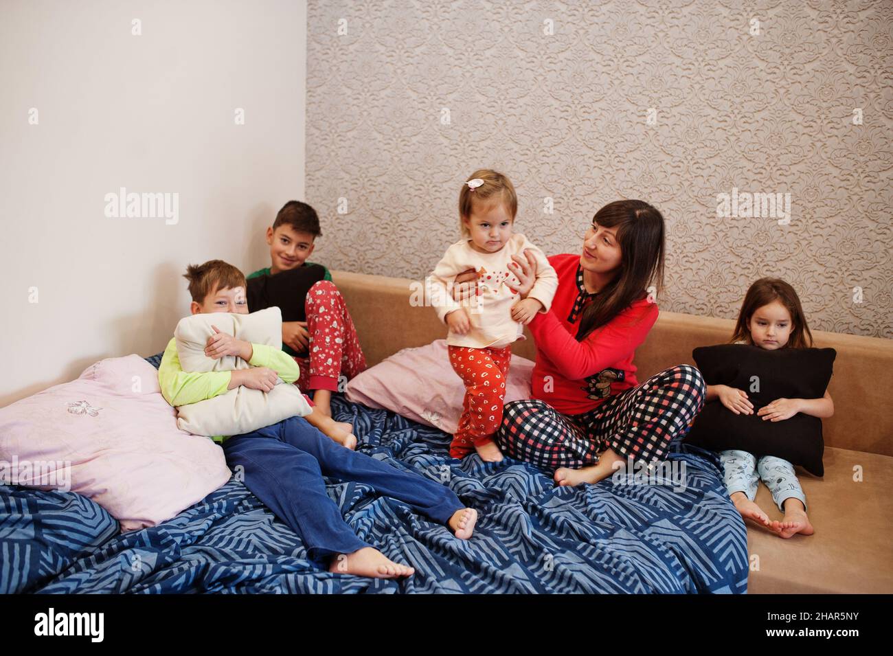 Happy big family is having fun together in bedroom. Large family morning concept. Mother with four kids wear pajamas in bed at home. Stock Photo