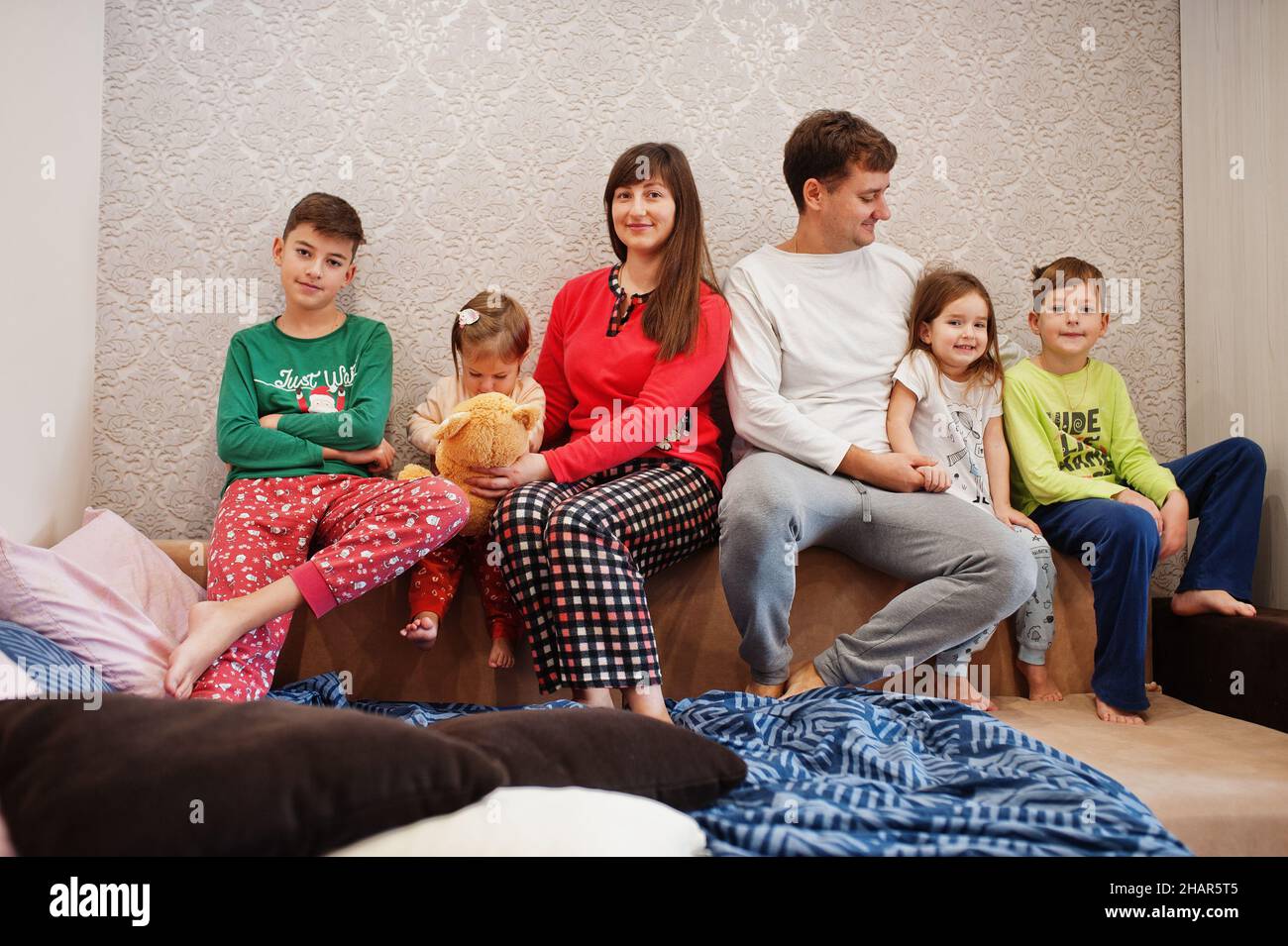 Happy big family is having fun together in bedroom. Large family morning concept. Four kids with parents wear pajamas in bed at home. Stock Photo