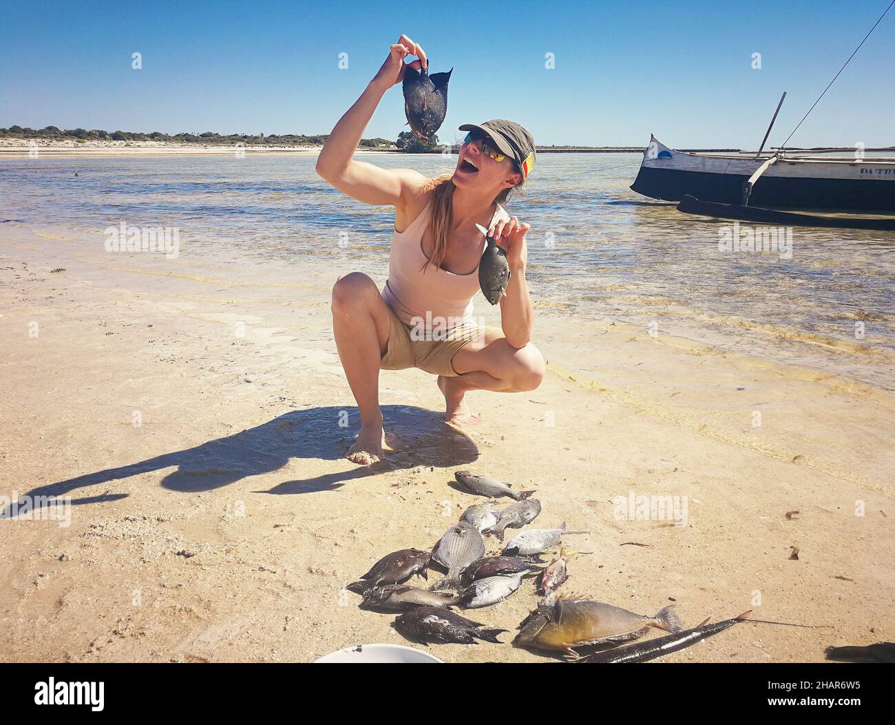 Young woman in shorts and t shirt posing with freshly caught sea fish, holding it near mouth Stock Photo