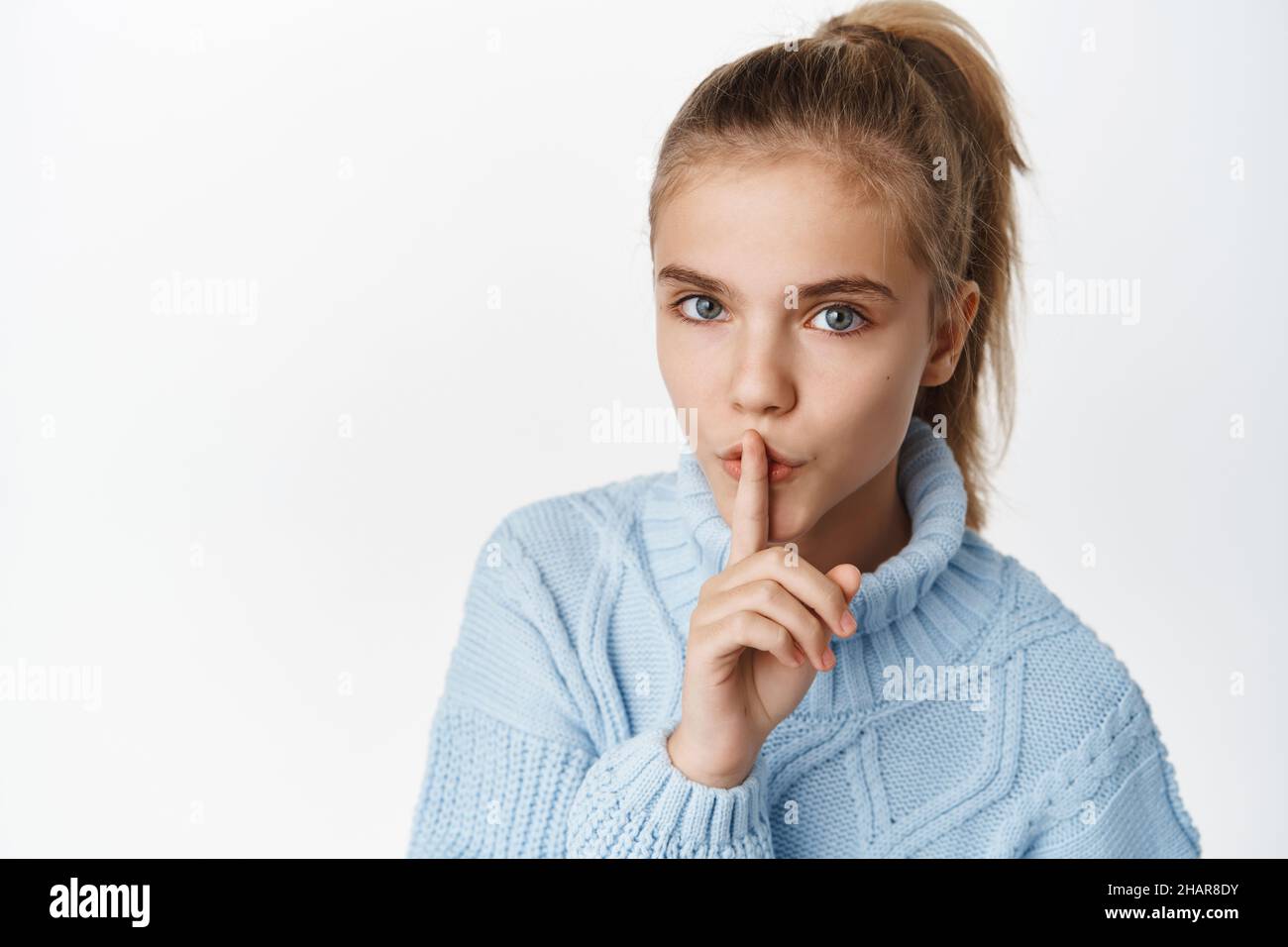 Close up portrait of beautiful little teen girl, shows hush, taboo quiet gesture, tell secret, press one finger to lips and say shh, stands in winter Stock Photo