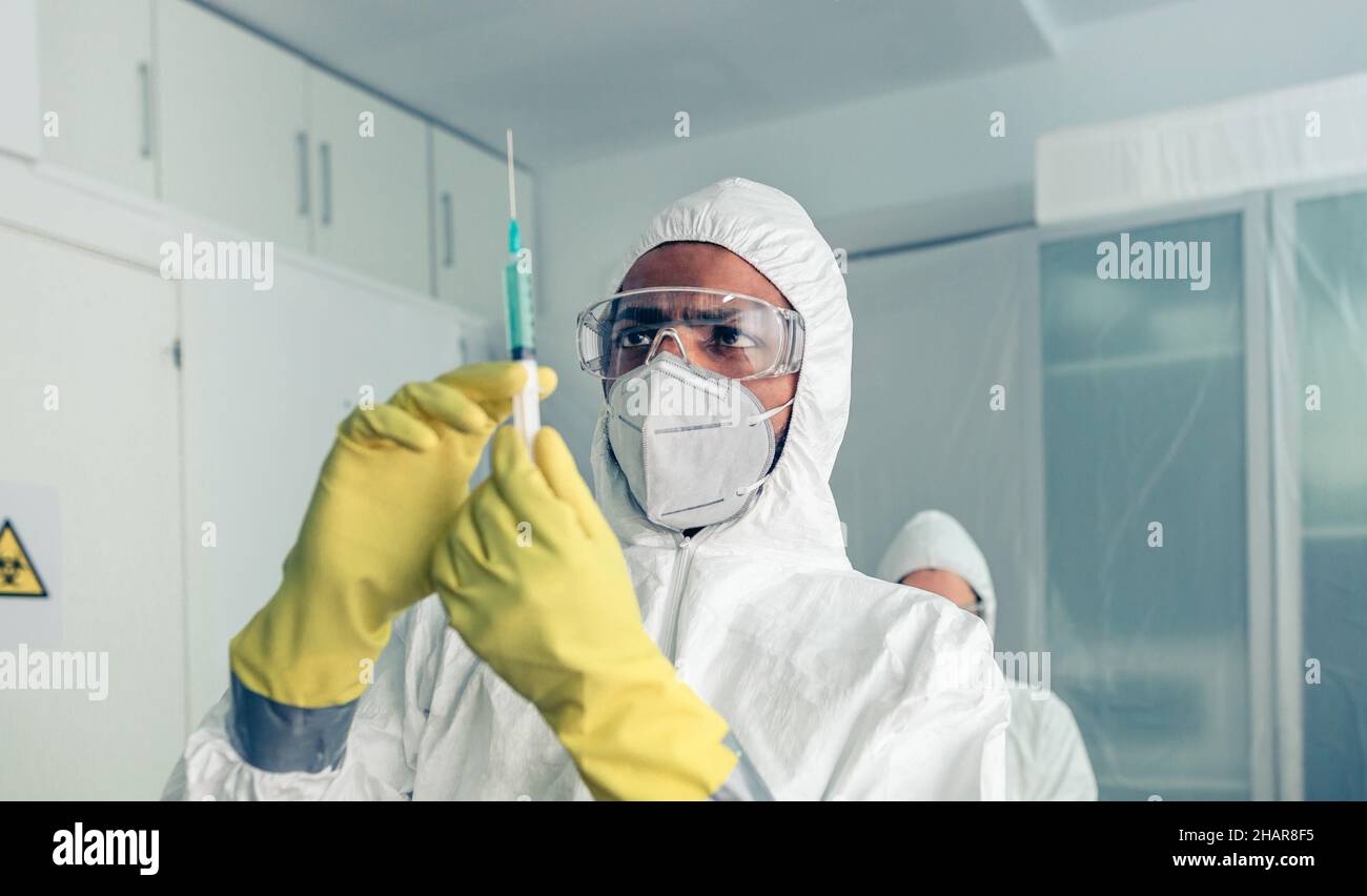 doctor in protective suit looking and preparing syringe with vaccine Stock Photo
